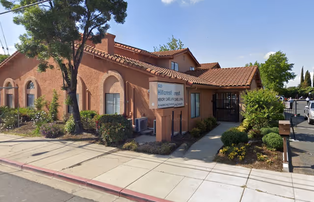 Exterior view of a tan stucco senior living facility with landscaping.