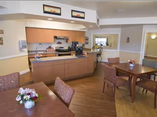 Shared dining area with tables and floral centerpieces facing a kitchen/serving counter and seating.