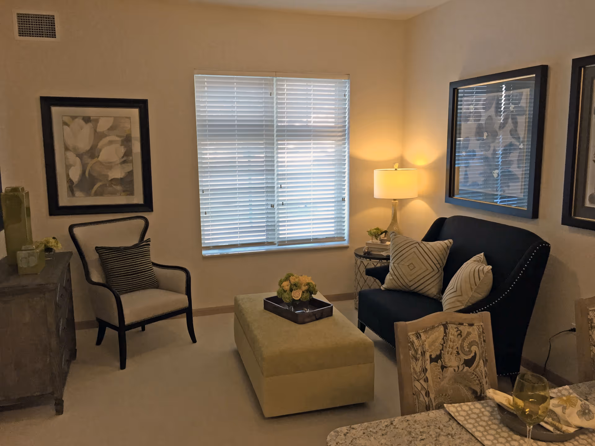Comfortable living room with a navy loveseat, armchair, ottoman, window blinds and wall art.