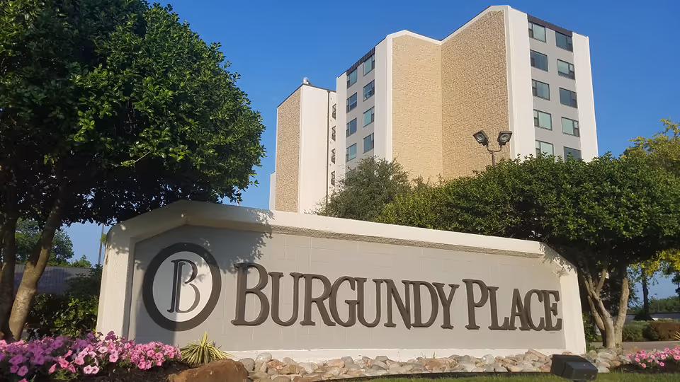 Exterior view of Burgundy Place entrance sign with a tall building behind.