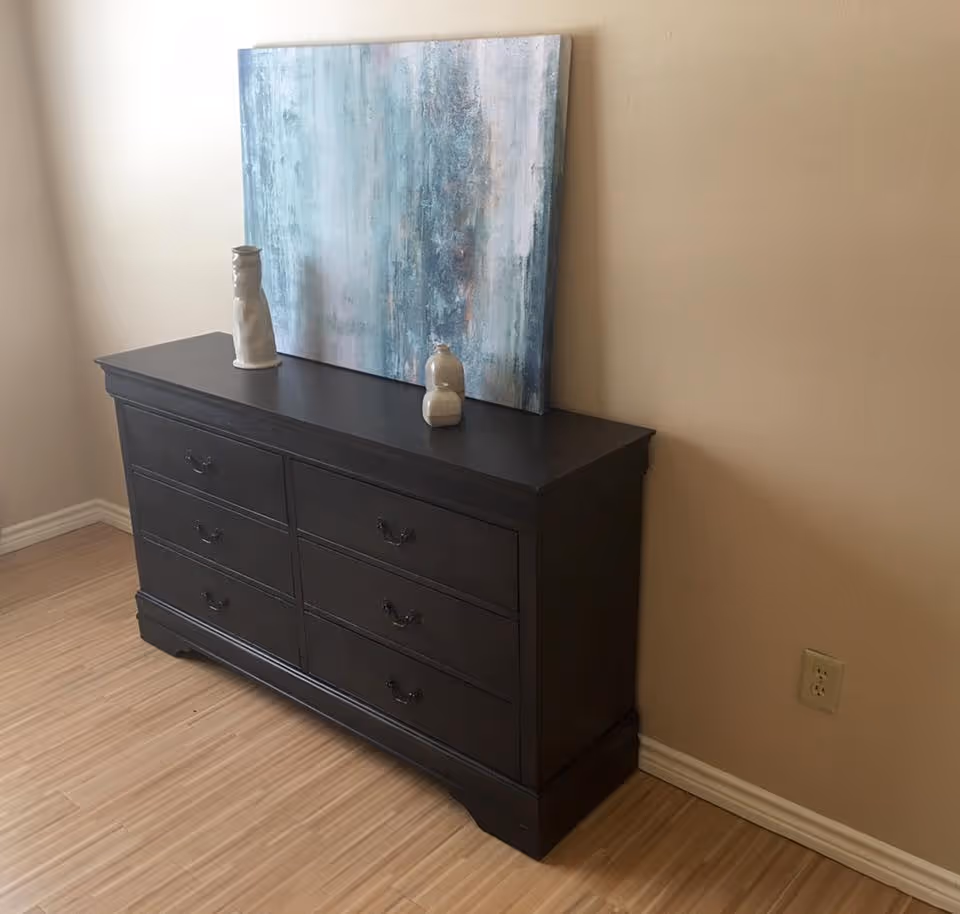 Dark wooden dresser against a beige wall with a blue abstract painting and two ceramic vases on top.