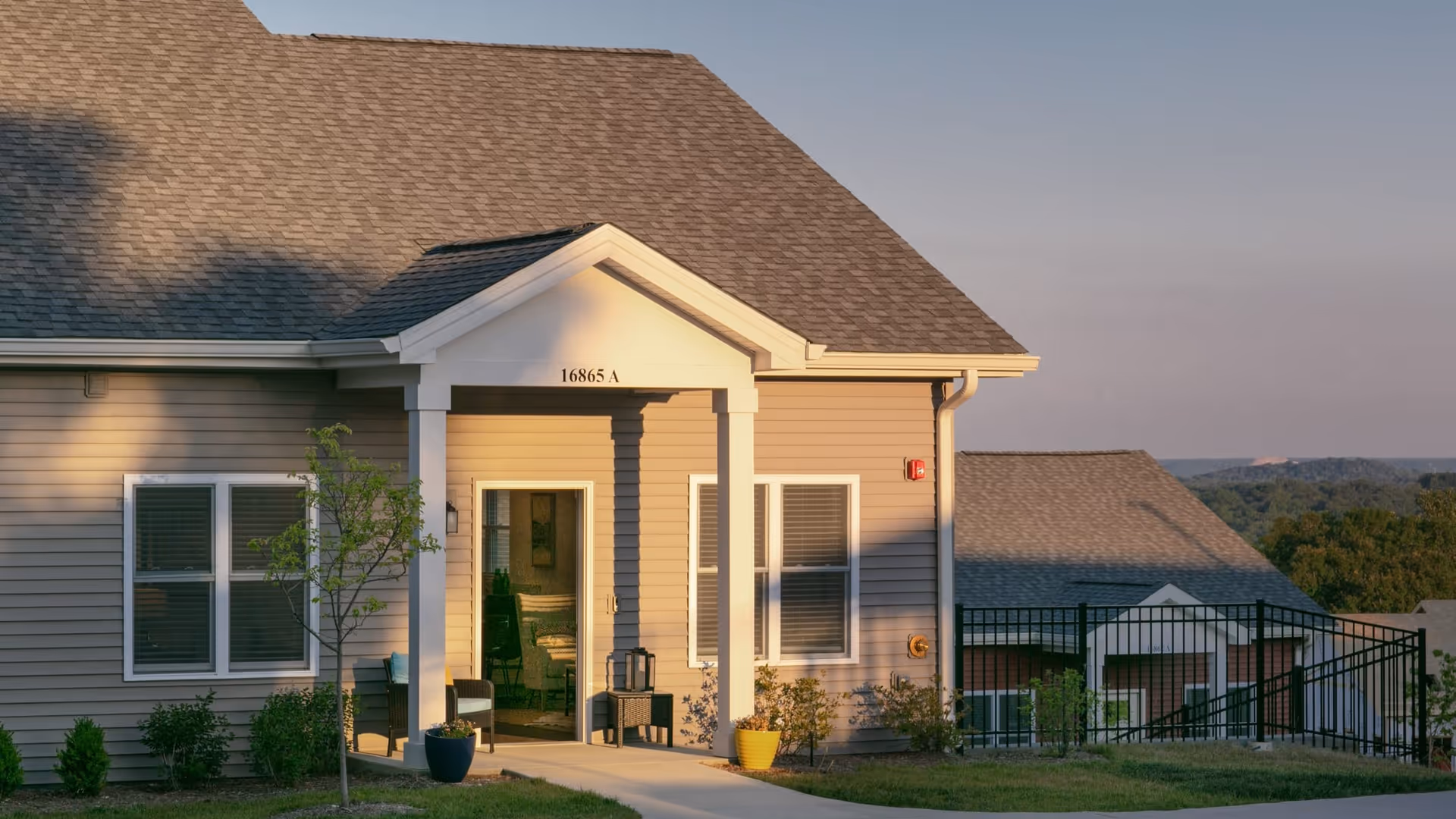 Covered front entrance of a single-story unit showing address '16865 A', potted plants, a small porch, and surrounding landscaping.