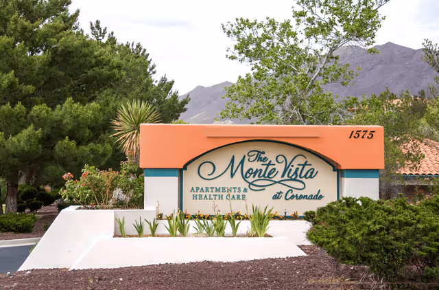 Entrance sign reading 'The Monte Vista at Coronado Apartments & Health Care' set in landscaped grounds with trees and mountains in the background.
