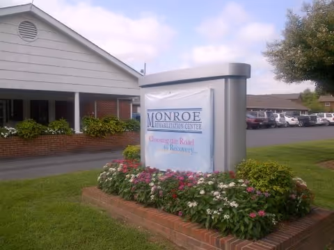 Front exterior of Monroe Rehabilitation Center with landscaped sign and parking lot.