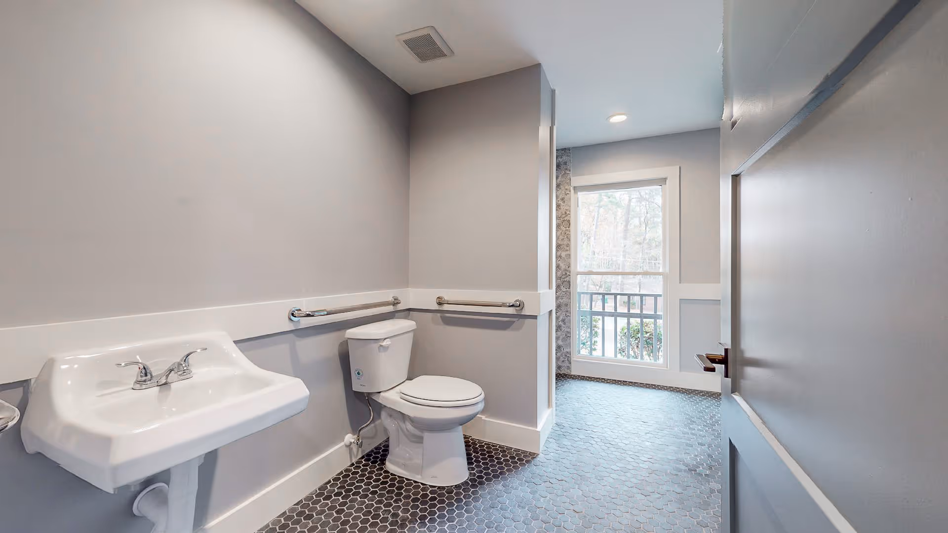 Accessible bathroom with a wall-mounted sink, toilet, grab bars, and a windowed doorway to an exterior space.