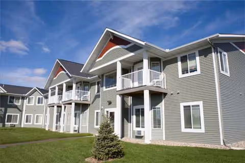 Exterior view of a gray multi-unit senior living building with balconies and green lawn.