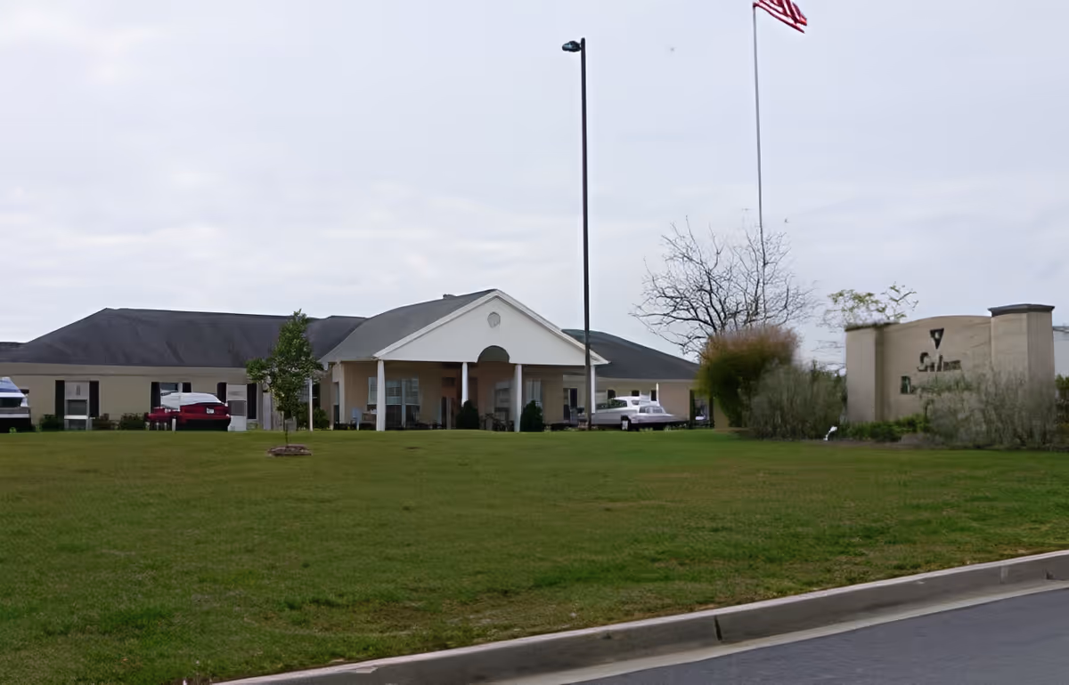 Exterior view of Salem Residential Care Facility showing a single-story building with a covered entrance, a flagpole with an American flag, a grassy lawn, and a sign with the facility's name near the road.