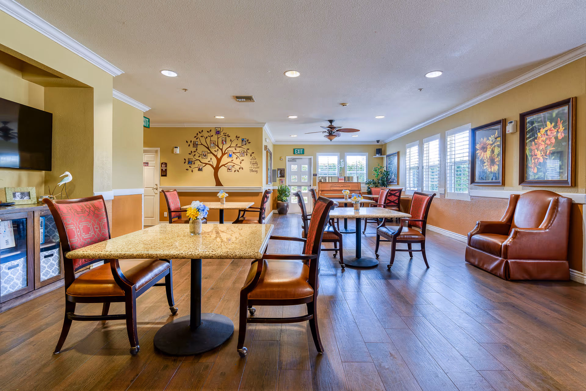 Spacious senior living dining room with tables and chairs, comfortable seating, wall art, and large windows.