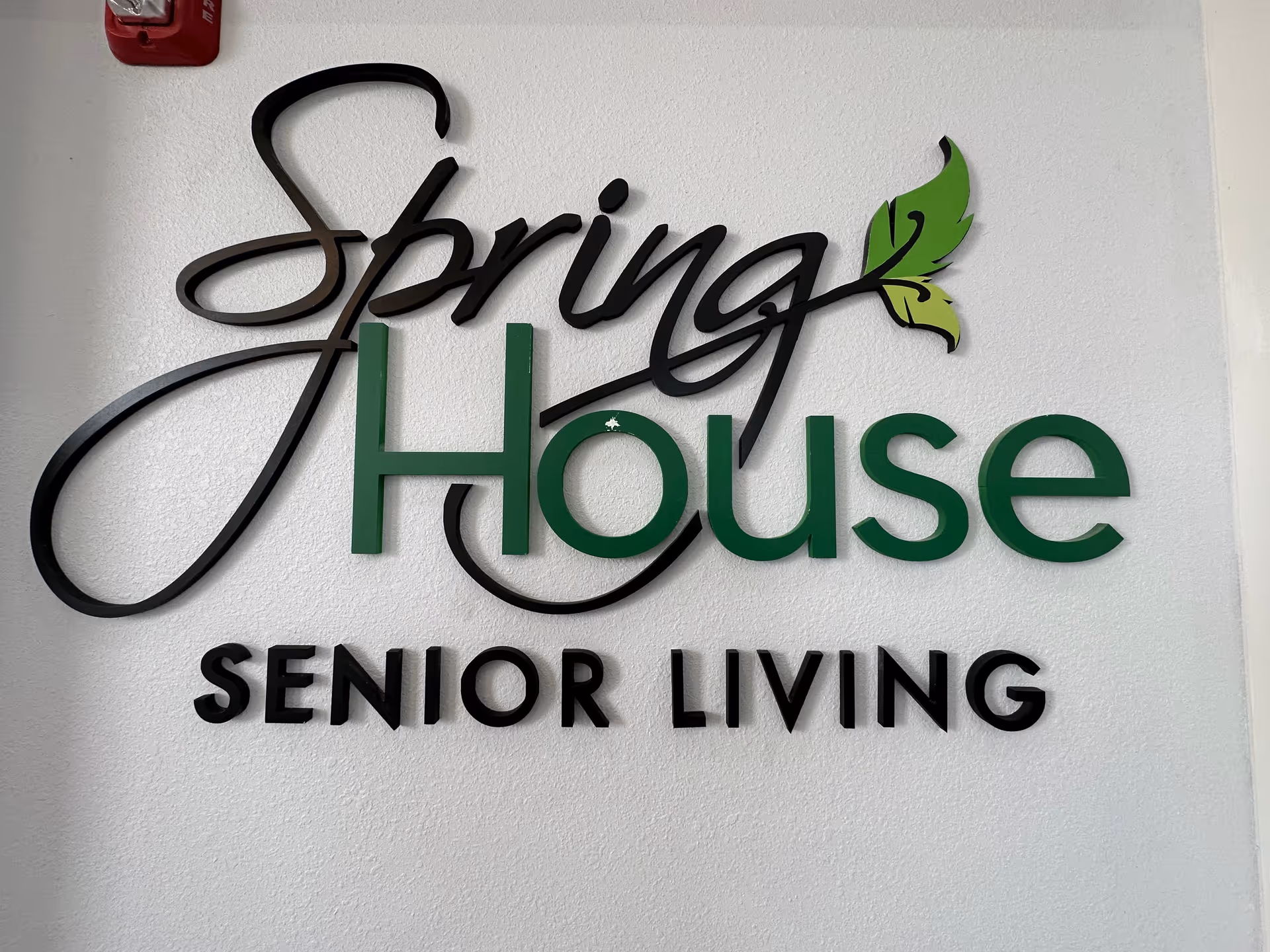Wall-mounted decorative sign reading "Spring House Senior Living" with a green leaf accent on a white wall.