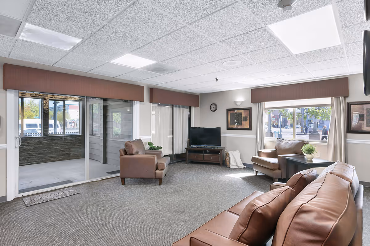 Bright communal living room with leather sofas and chairs, a TV on a stand, large windows and a sliding glass door to an enclosed porch.