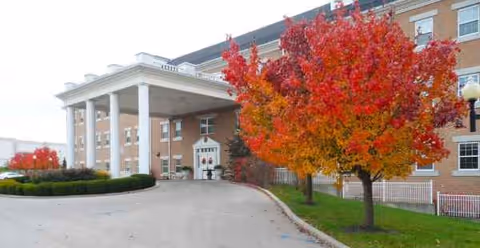Front entrance of a brick assisted living building with red autumn trees.