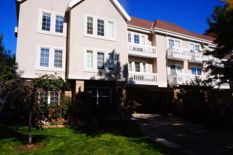 Exterior view of a beige, multi-story senior living building with balconies and a lawn.
