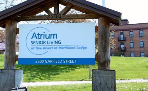 Outdoor sign for Atrium Senior Living at Northland Lodge beside a grassy front lawn.