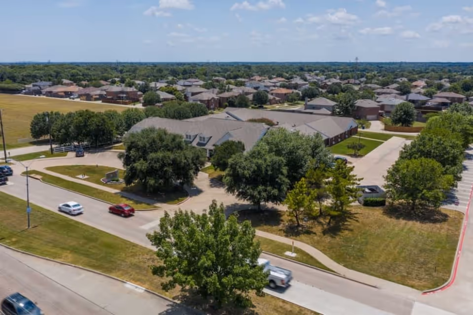 Aerial exterior view of the Meadow Creek Senior Living building surrounded by trees, parking areas and nearby houses.