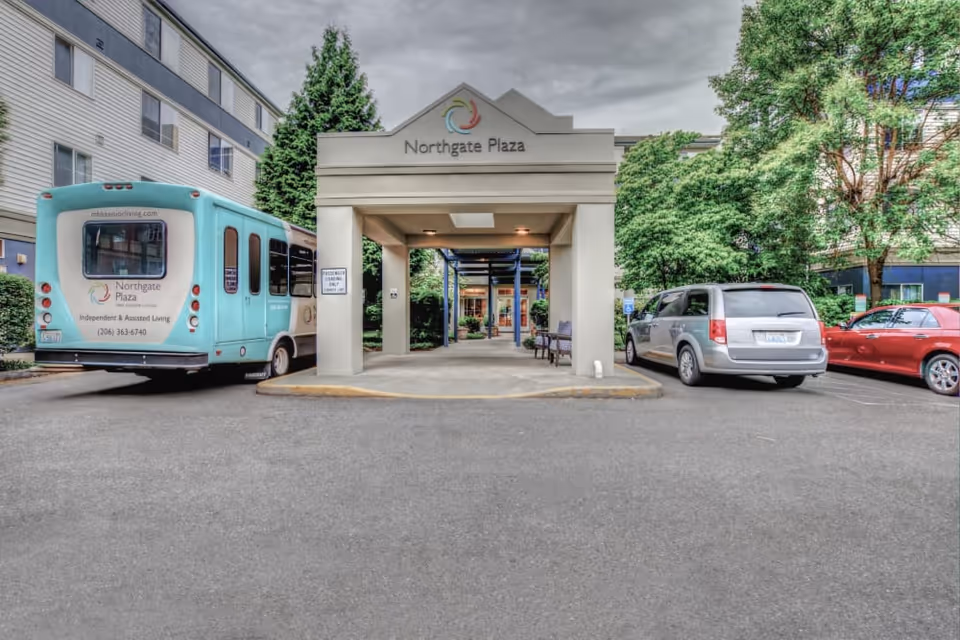 Entrance canopy of the Northgate Plaza senior living facility with a shuttle bus and parked cars in the driveway.