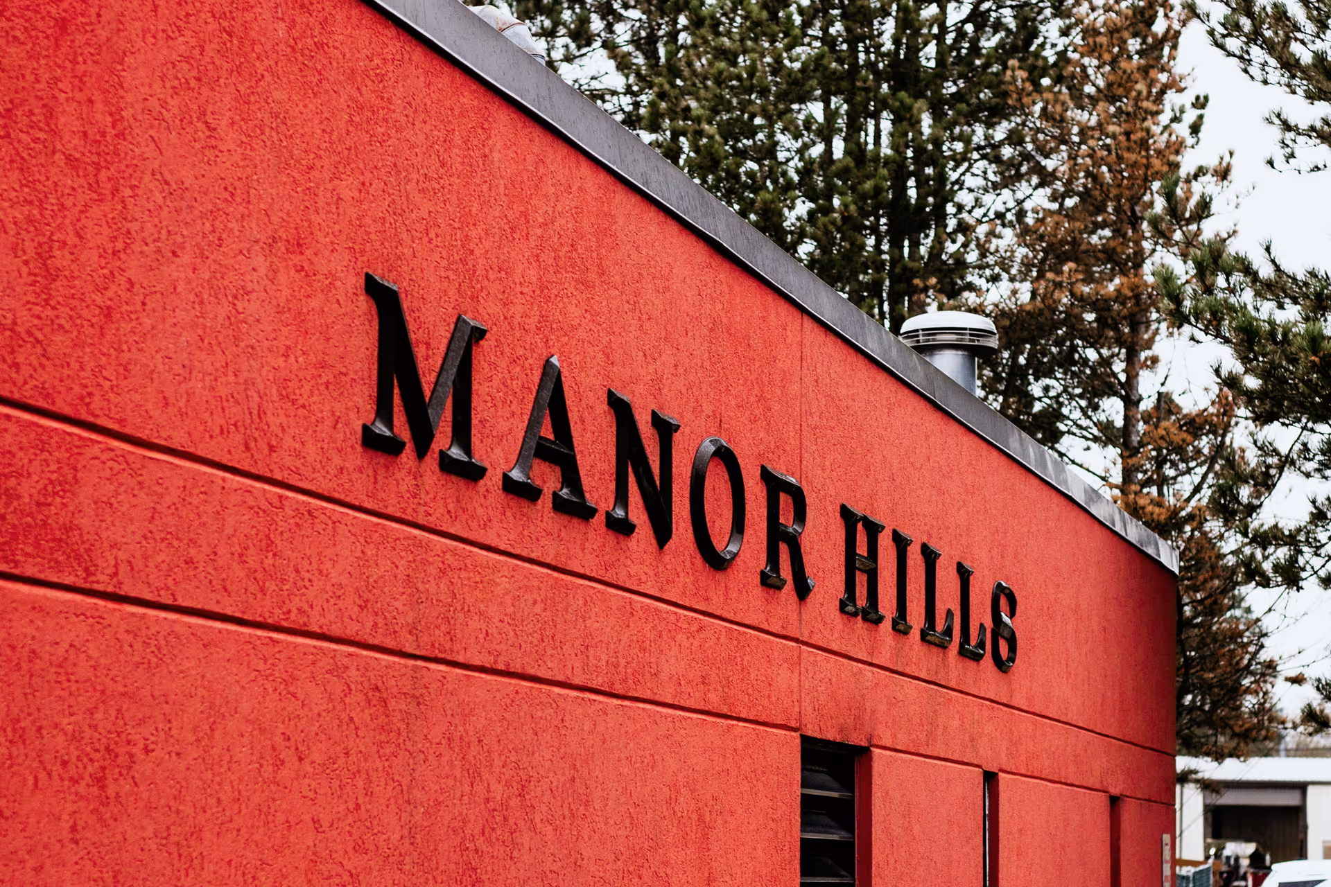 Red exterior wall with large black MANOR HILLS sign on the building.