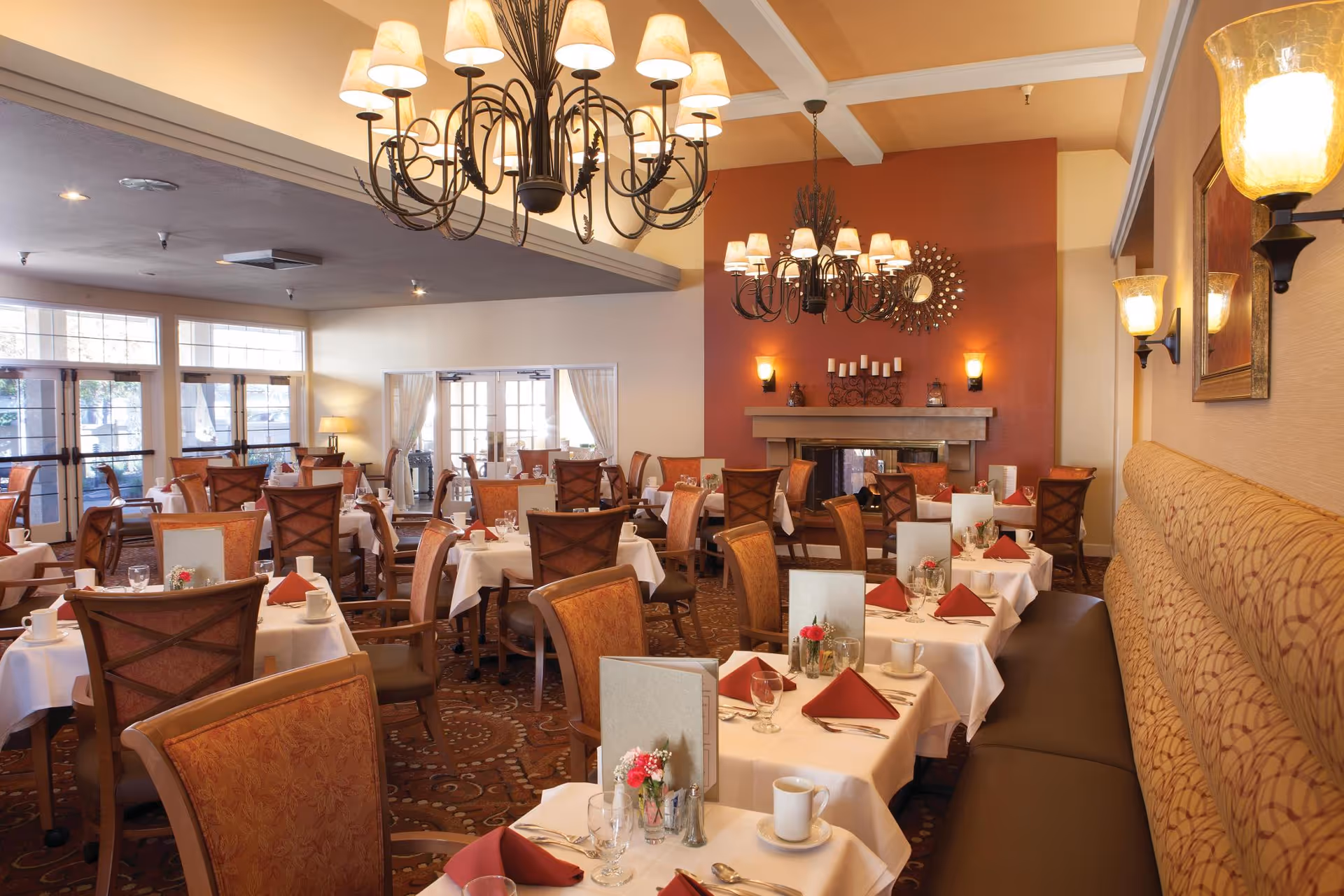 Elegantly furnished dining room with neatly set tables, chandeliers, and warm lighting.
