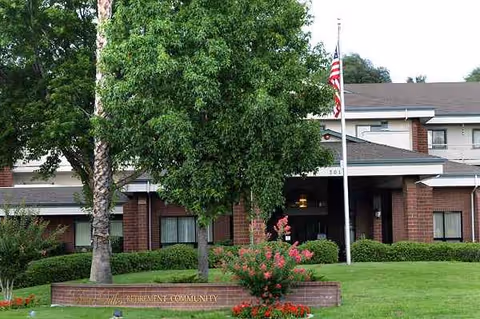 Front view of River Commons Senior Living, brick entrance with flagpole and landscaped lawn.