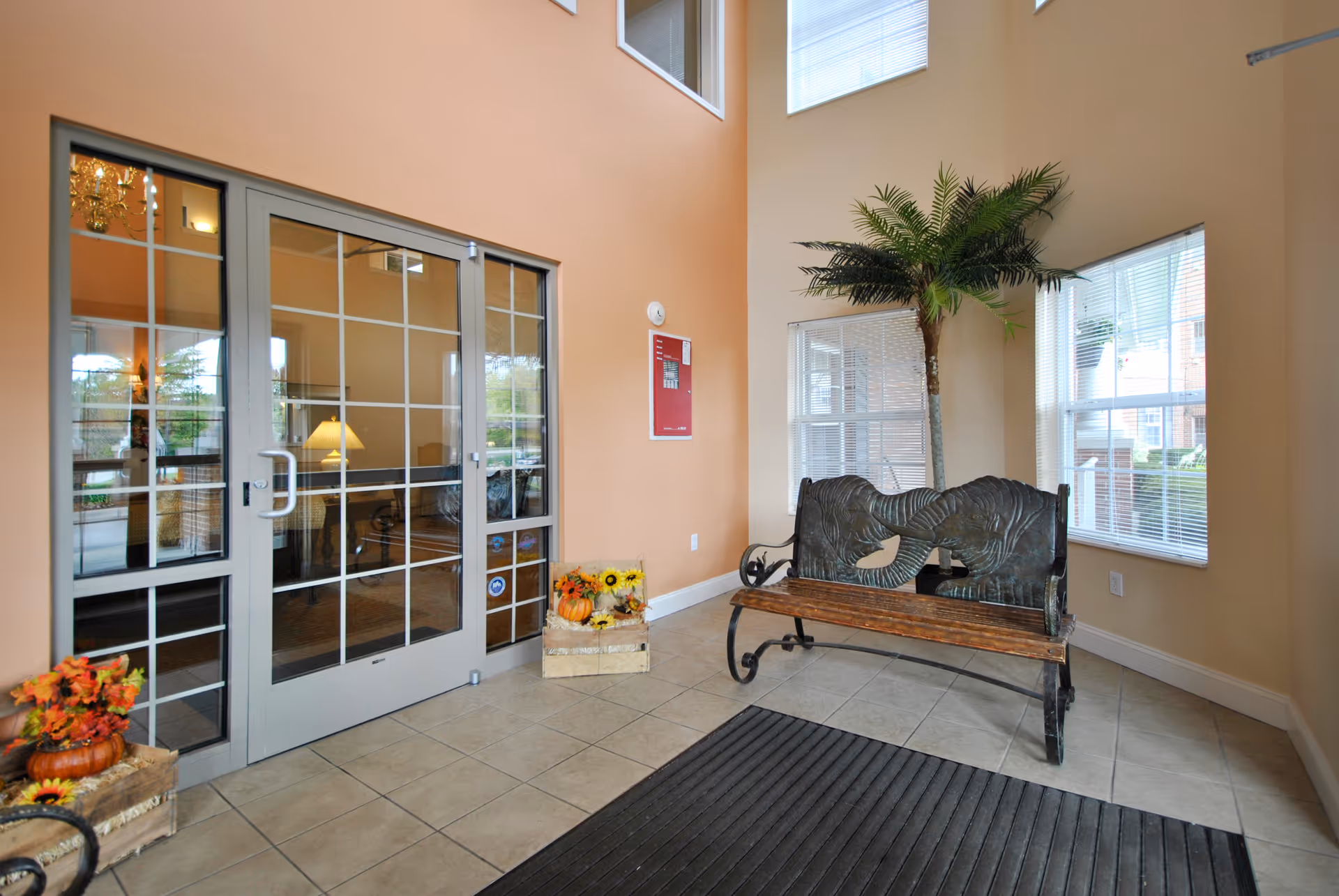 Entry foyer with glass double doors, a decorative metal-and-wood bench, a potted palm, and seasonal decorations.