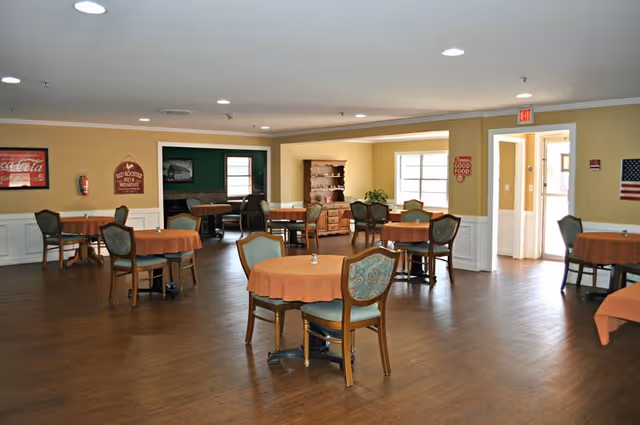 Spacious dining room with round tables covered in orange tablecloths and chairs on wood flooring.