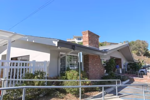 Single-story senior care facility exterior with ramp, brick accents, and landscaped shrubs.