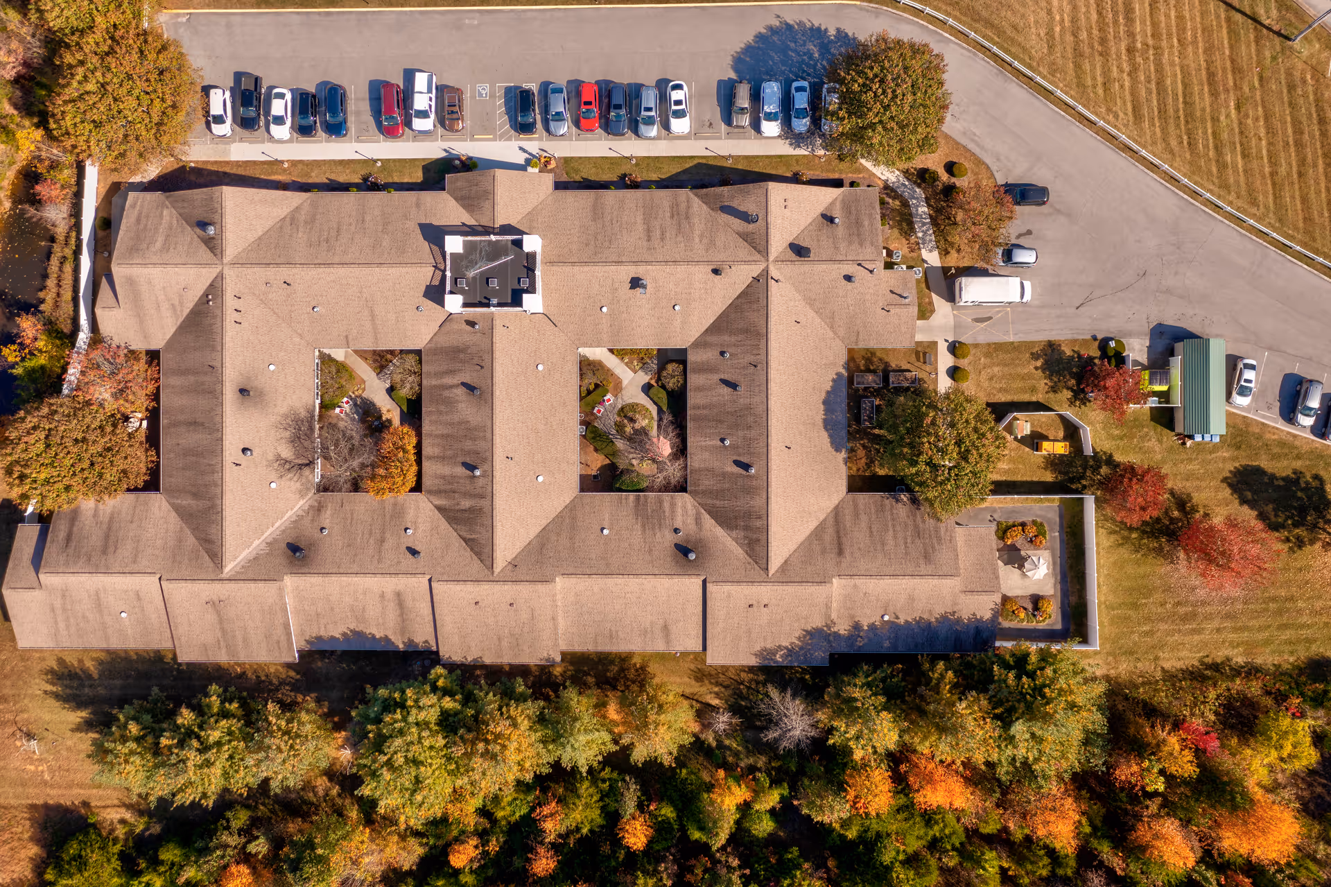 Aerial top-down view of a senior living complex building with parked cars, driveways, and surrounding autumn trees.
