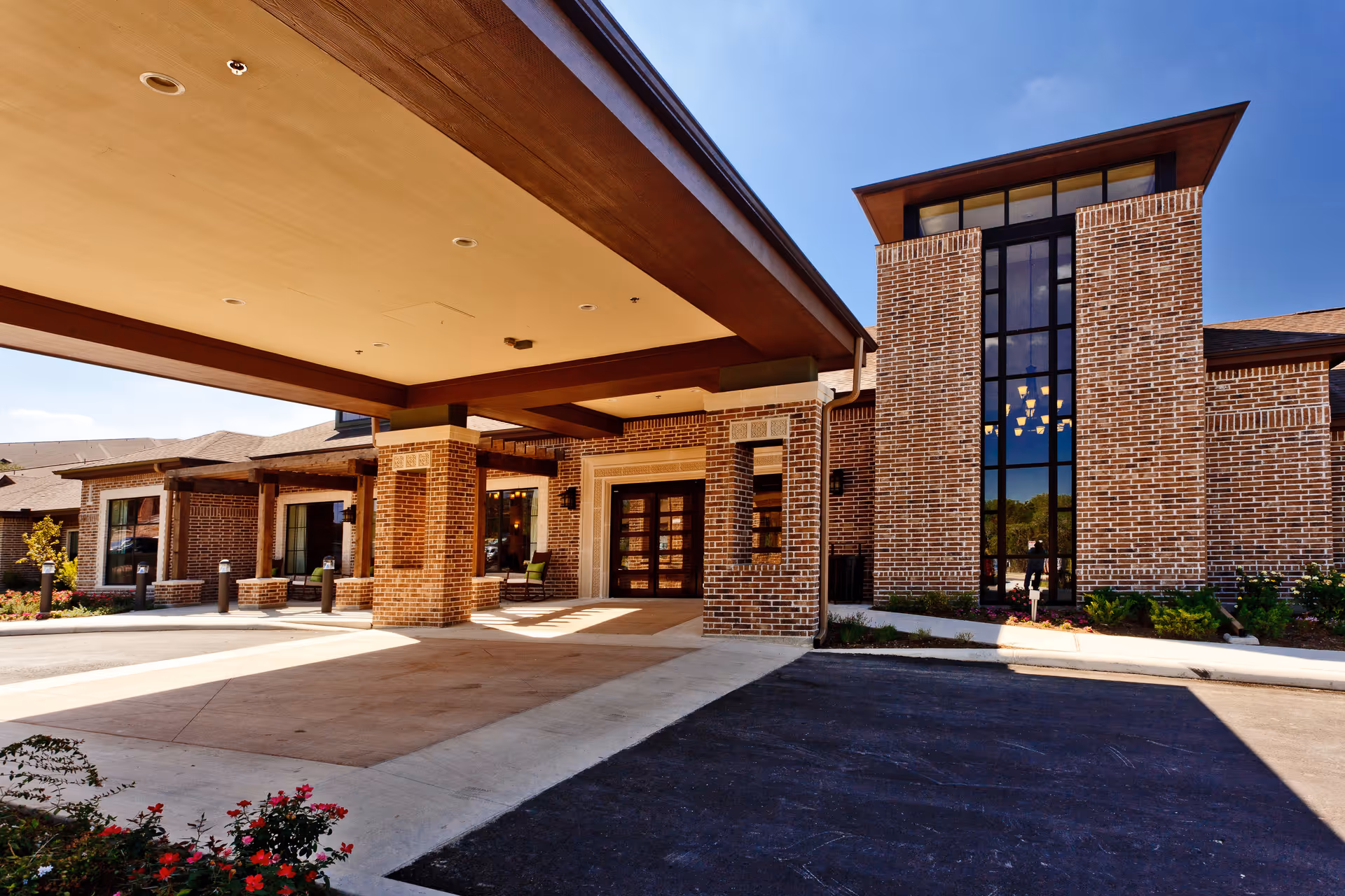 Exterior view of the entrance to a brick building with large windows and a covered drop-off area, under a clear blue sky.