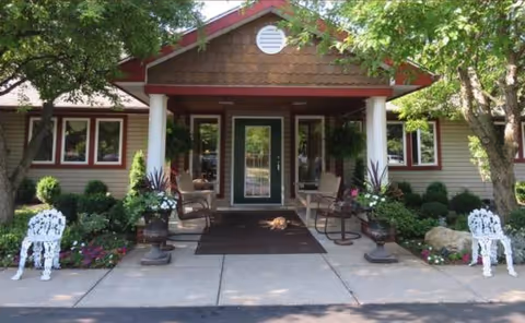 Front entrance of Heritage Manor of Lockport with potted plants, chairs, and a dog.