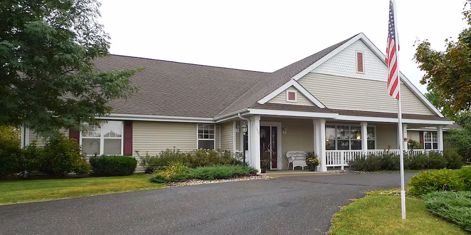 Single-story senior living facility front with porch, flagpole, and landscaped entrance.