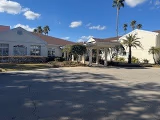 Exterior view of a single-story building with a covered entrance, palm trees, and a clear blue sky with some clouds.