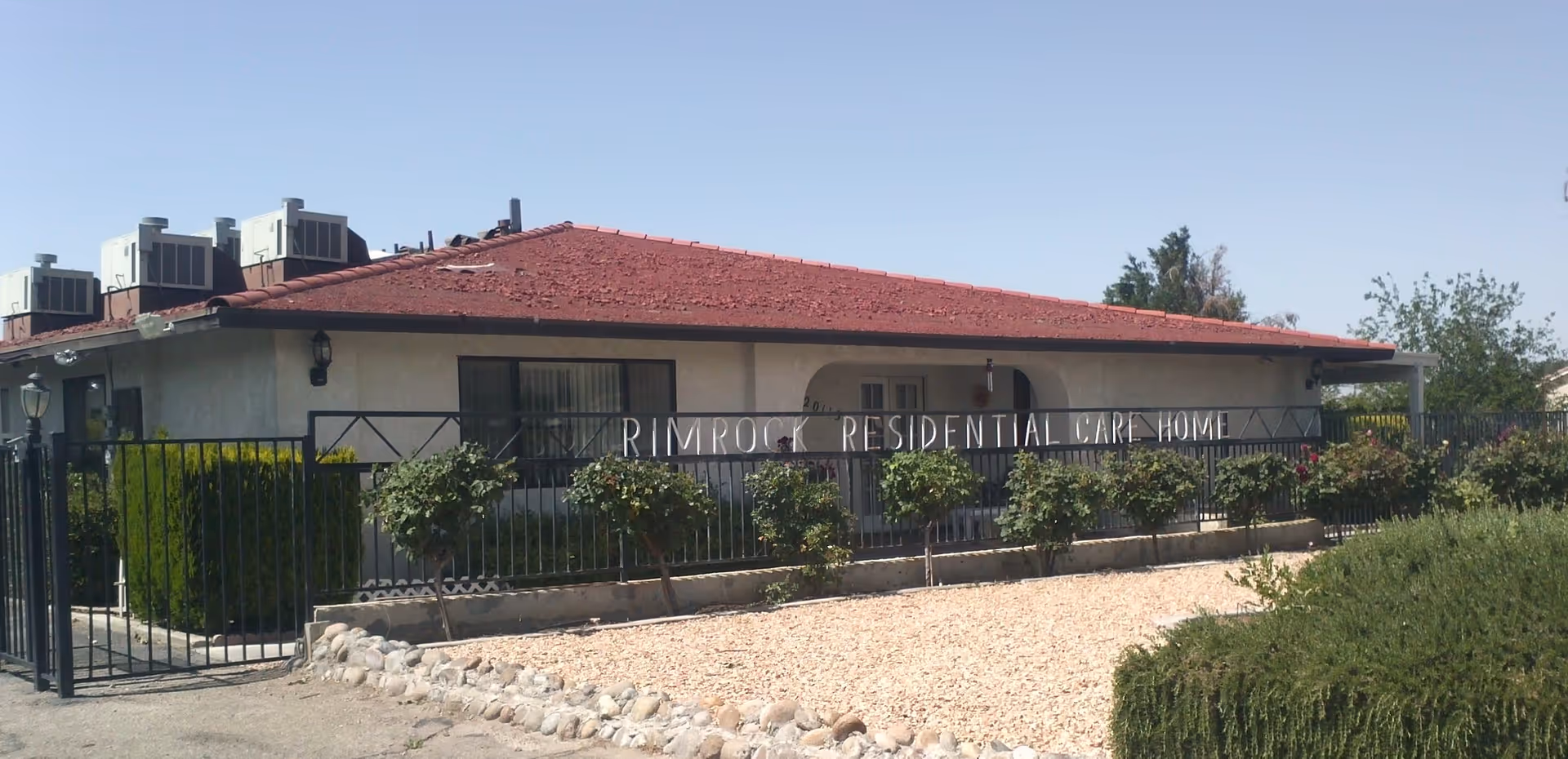 Single-story residential care home with a red roof, front fence and sign reading Rimrock Residential Care Home.