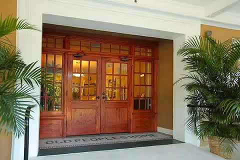 Wooden double doors frame the entrance to a senior living facility with potted plants.