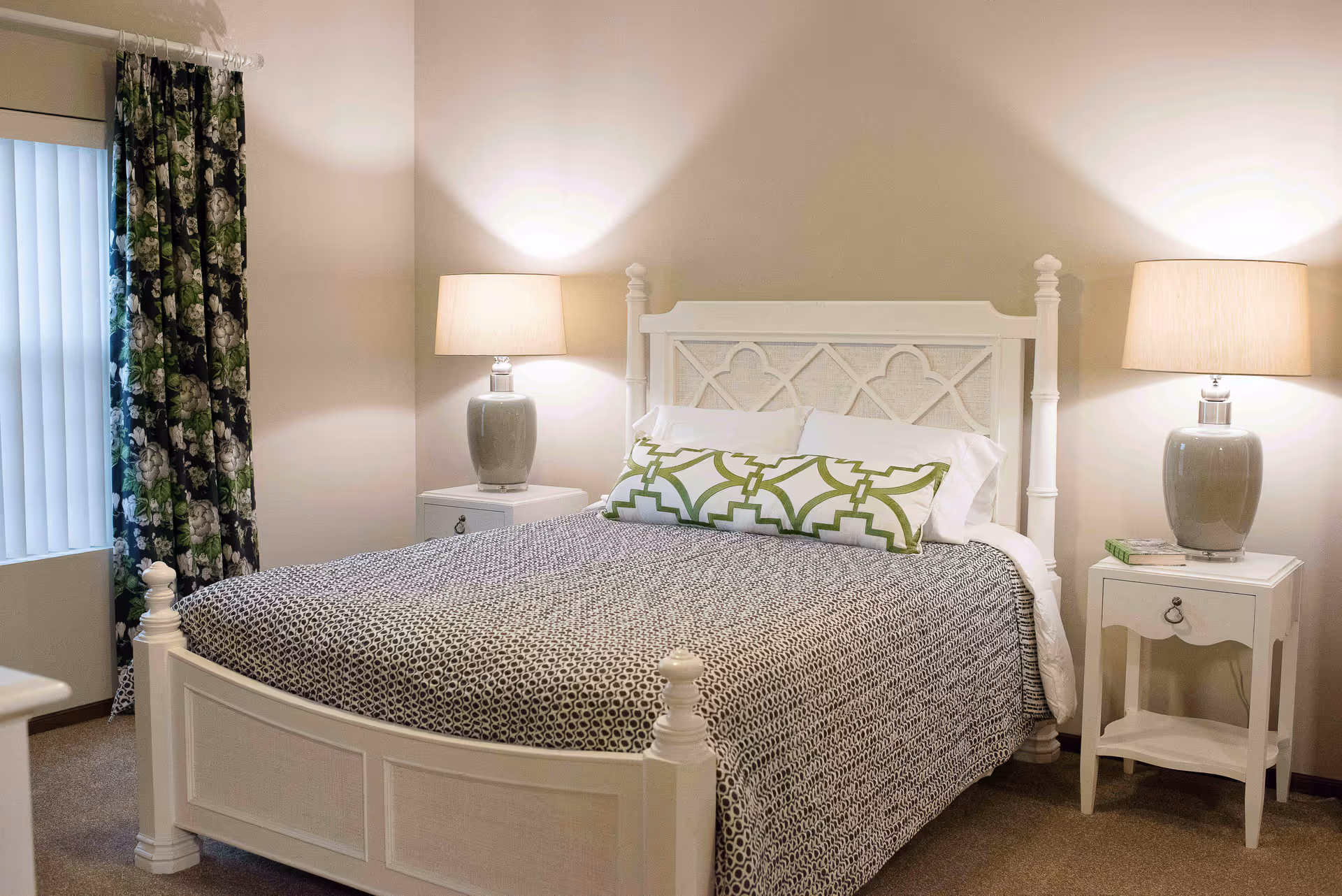A neatly made bedroom with a white wooden bed, patterned bedding, decorative pillows, and two bedside tables with lamps.