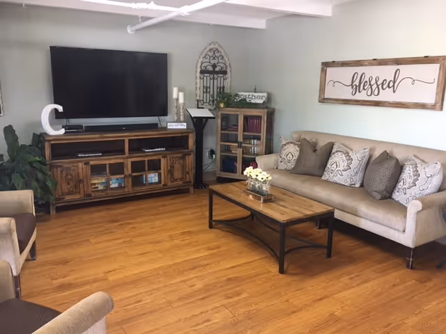 Bright lounge with a sofa, coffee table, large TV on a wooden console, and a framed 'blessed' sign on the wall.