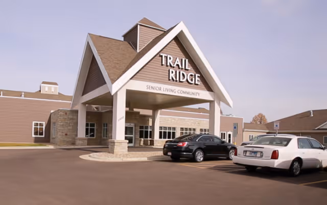 The front entrance and porte-cochere of the Trail Ridge Senior Living Community building with a few parked cars in the driveway.