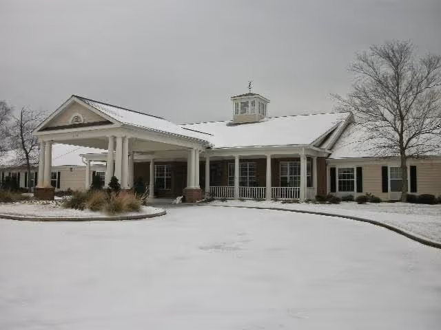 Snow-covered front entrance of a single-story senior living building with a columned portico and small cupola.