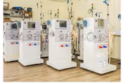 A clinical room with a row of dialysis machines positioned on a wood‑tone floor.