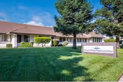 Single-story healthcare center building with a manicured lawn, trees, and a sign reading 'Diamond Ridge HealthCare Center' under a blue sky.