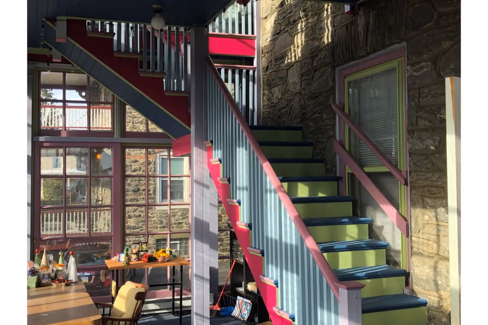Interior of Roxborough Home for Women with a colorful staircase beside stone walls and a table.