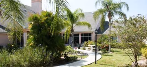 Curved walkway leads to the Brookdale Cape Coral entrance with palm trees and landscaping.