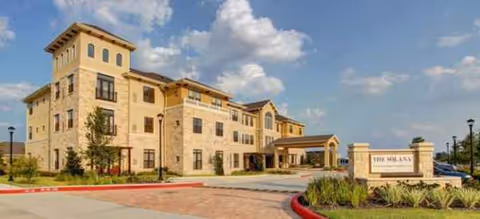 Stone-facade senior living building with a covered entrance and manicured landscaping.