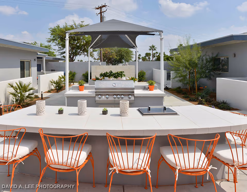 Outdoor courtyard with a built-in grill and a tiled countertop bar with orange chairs under a canopy.
