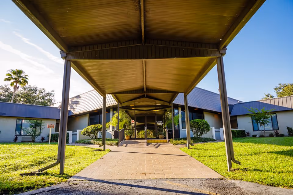 Entrance of Solaris HealthCare Plant City building with a covered walkway, green lawn, bushes, and trees under a clear blue sky.