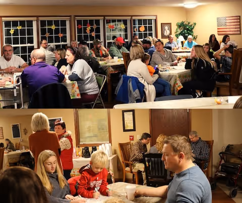 Numerous people seated at tables in a communal dining room, socializing and eating.