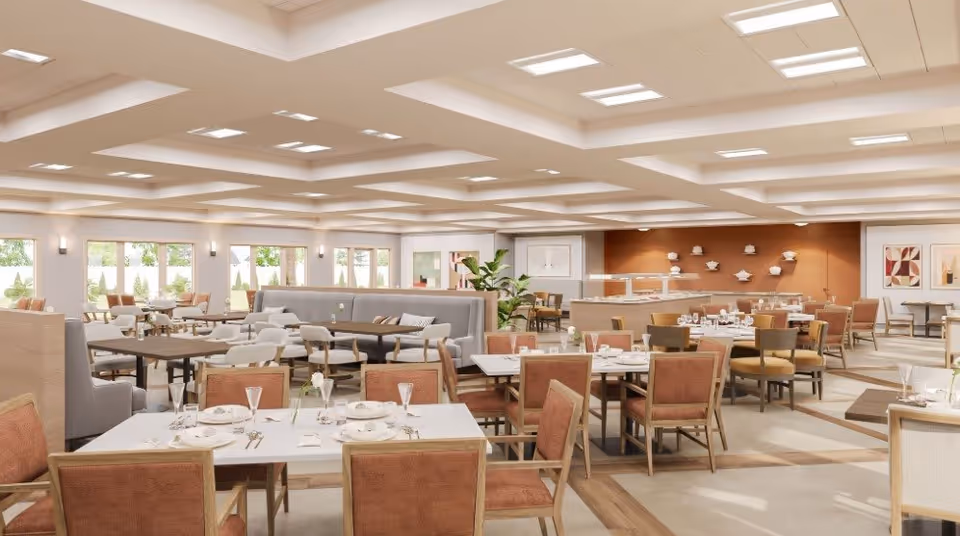 A spacious and well-lit dining room with multiple tables and chairs arranged neatly. The tables are set with plates, glasses, and cutlery. The room features large windows allowing natural light to enter, modern ceiling lights, and a warm color palette with beige and brown tones. There are decorative elements on the walls and a buffet area in the background.