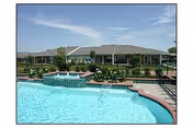 Outdoor swimming pool with a raised spa in the foreground and single-story apartment buildings and landscaping in the background.