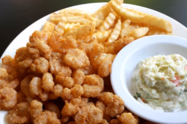 A white plate with crispy fried popcorn shrimp, crinkle-cut French fries, and a small bowl of creamy coleslaw.