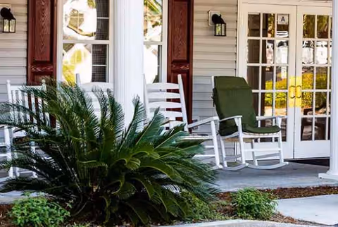 White front porch with rocking chairs, green cushions, and glass doors.