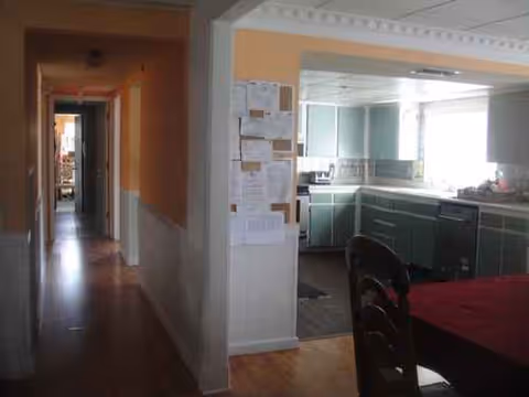 Hallway view of a senior living kitchen with mint-green cabinets and a dining table.
