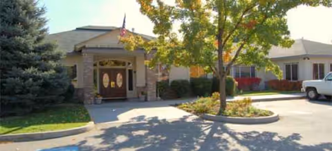 Senior living facility front entrance with driveway, trees, and landscaping.